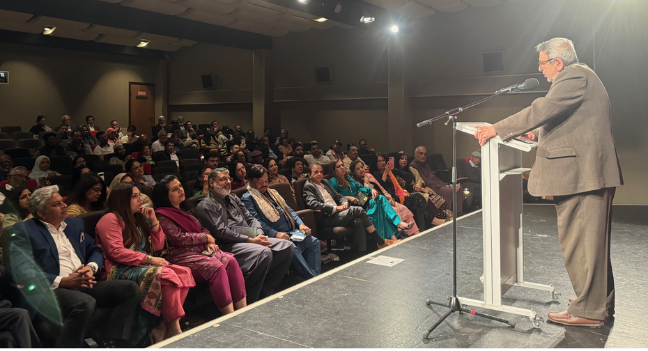 A person standing in front of a podium with a microphone and a crowd of people

Description automatically generated