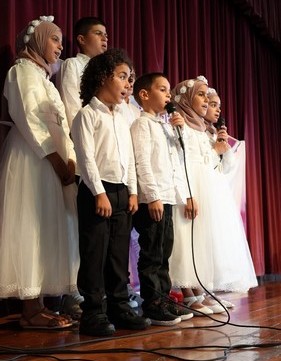 A group of children singing on stage

Description automatically generated