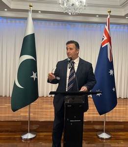 A person standing at a podium with flags behind him

Description automatically generated