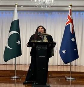 A person standing at a podium with flags behind her

Description automatically generated