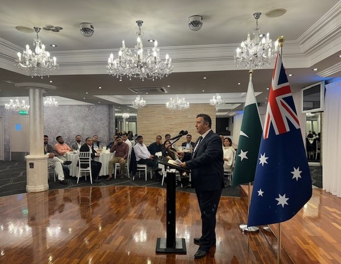 A person standing at a podium with flags in front of him

Description automatically generated