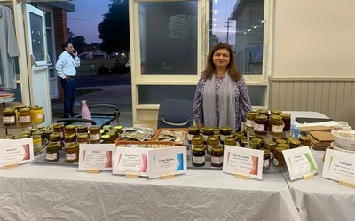 A person standing next to a table with jars of jam

Description automatically generated