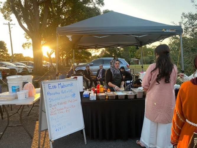 A group of people standing at a food stand

Description automatically generated