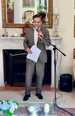 A person in a suit holding a microphone and paper

Description automatically generated