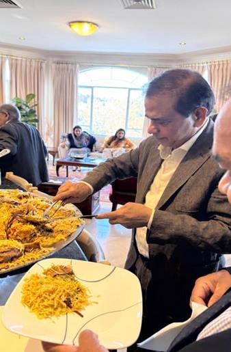 A person in a suit standing in front of a large plate of food

Description automatically generated