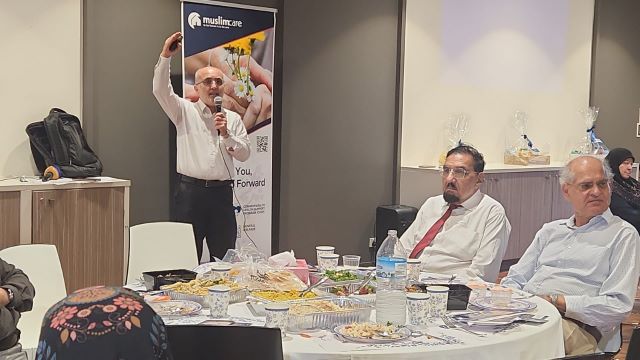 A person in a white shirt and red tie speaking into a microphone

Description automatically generated