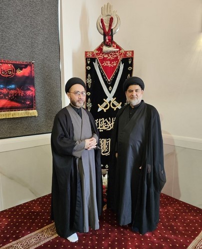 Two men standing in front of a large black and red cloth

Description automatically generated