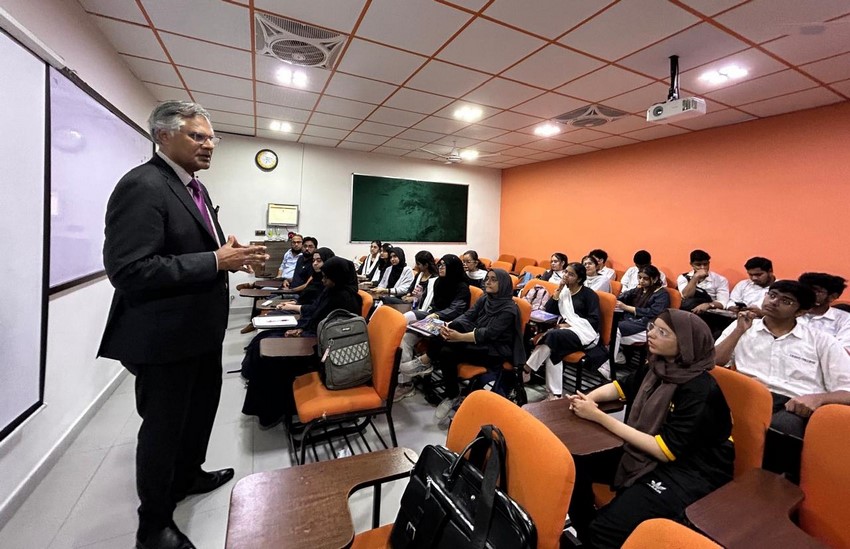 A person in a suit standing in front of a group of people in a classroom

Description automatically generated