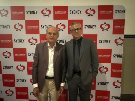 Two men standing in front of a wall with red and white signs

Description automatically generated