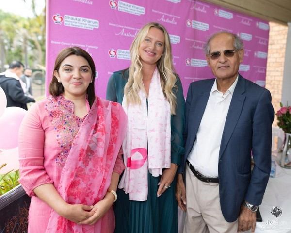 A group of people standing in front of a pink banner

Description automatically generated