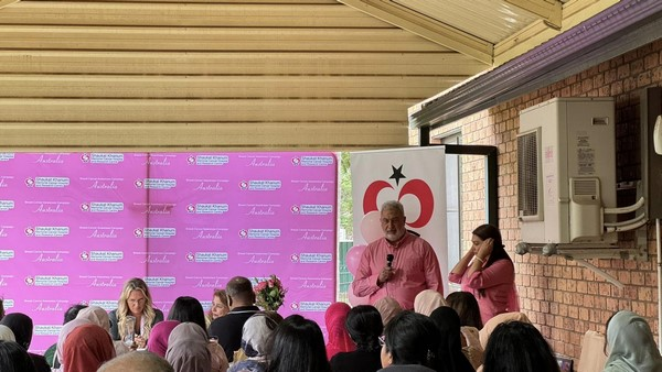 A person in pink shirt speaking to a crowd of people

Description automatically generated